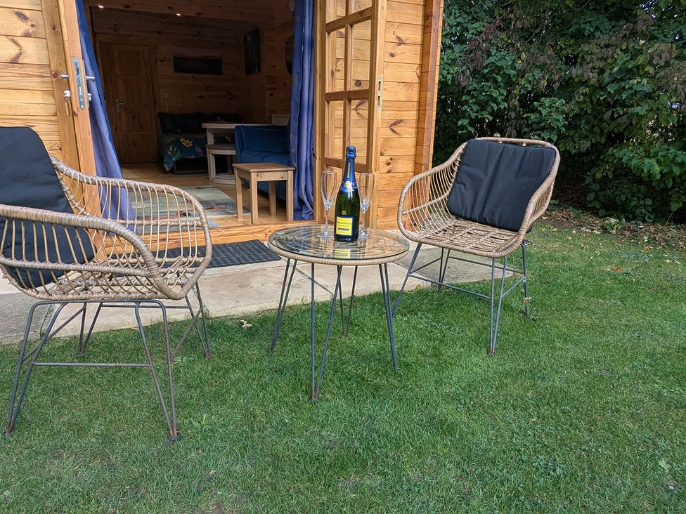 An outdoor seating area with two chairs and a table near a wooden cabin at Snowdrop Lodge Dog friendly Nr Anderby Creek Alford