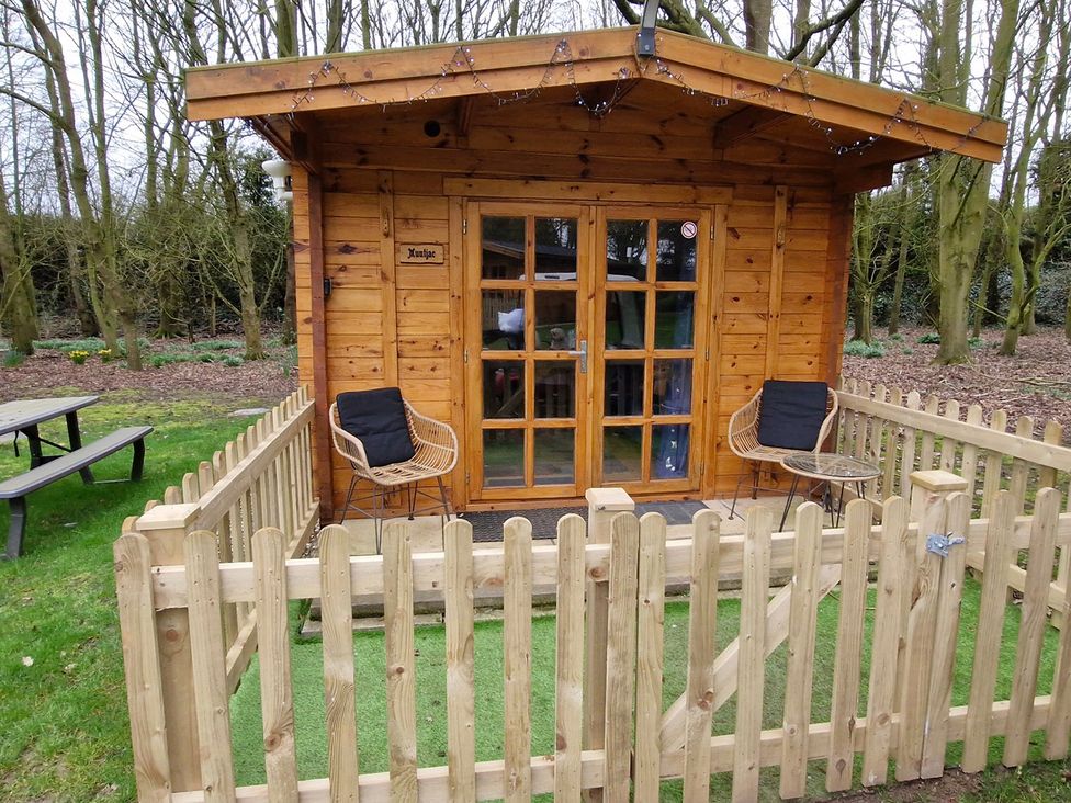 A wooden cabin with a fenced area and seating outside at Snowdrop Lodge Dog friendly Nr Anderby Creek, Alford