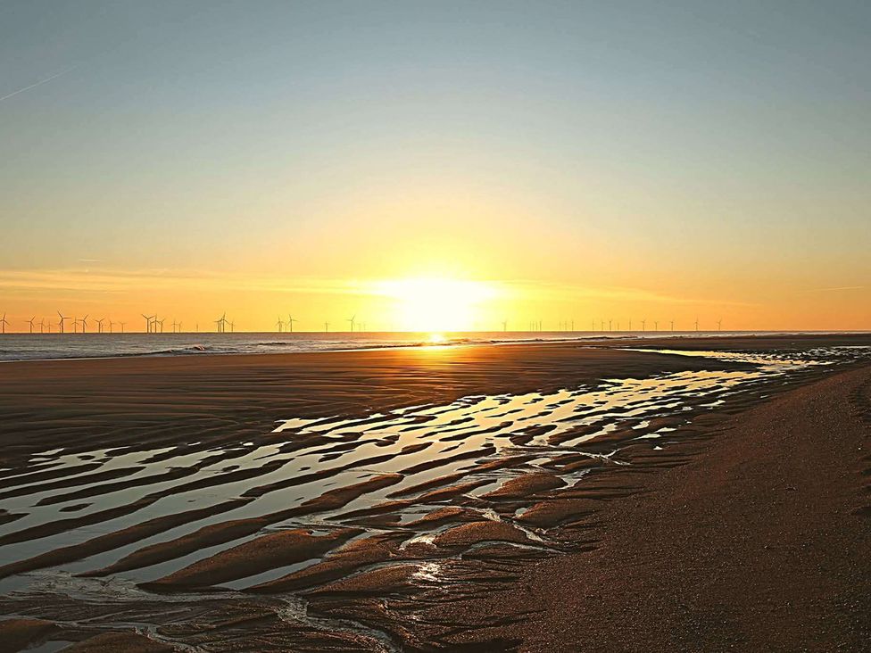 A beach at sunset with reflecting water and wind turbines in the background at Snowdrop Lodge Dog friendly Nr Anderby Creek Alford