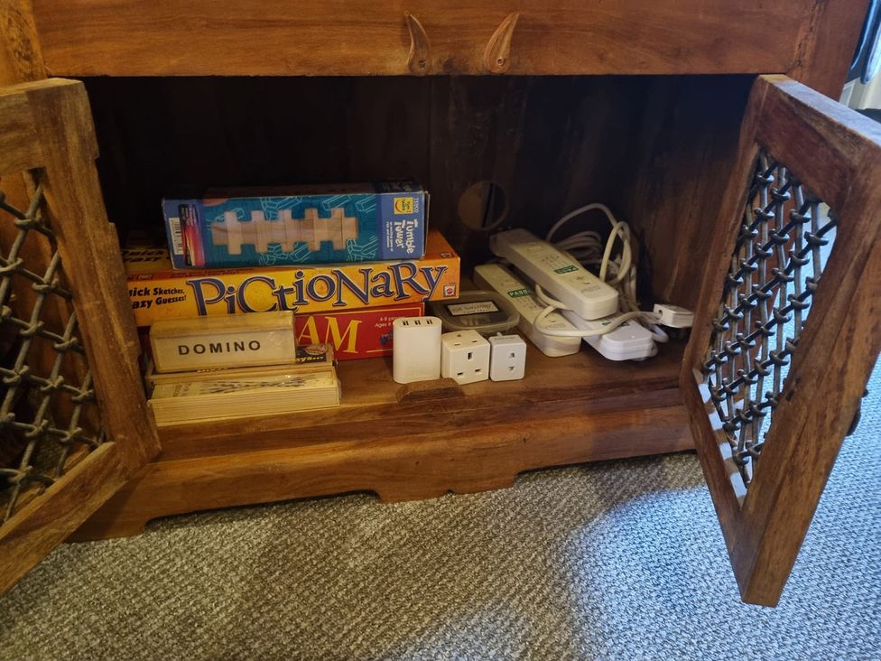 A wooden storage cabinet containing board games and electrical accessories at 2 bed Lodge near Dunoon on the Shore Front, Innellan near Dunoon