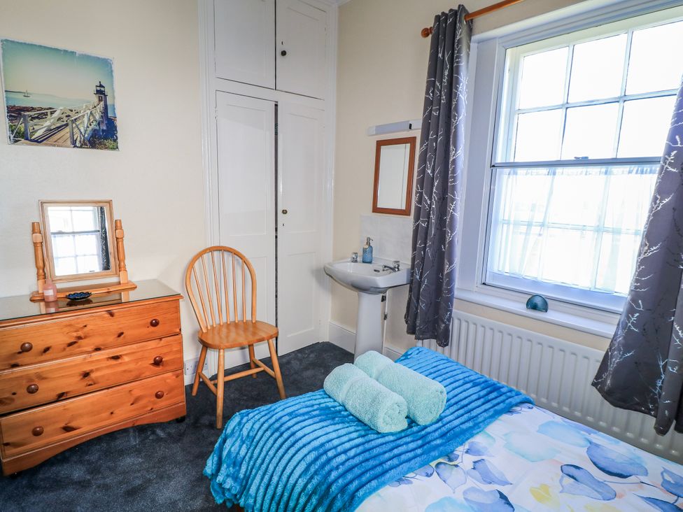 A bedroom with a bed, dresser, chair, mirror, and sink at Old Higher Lighthouse Stopes Cottage Portland Bill