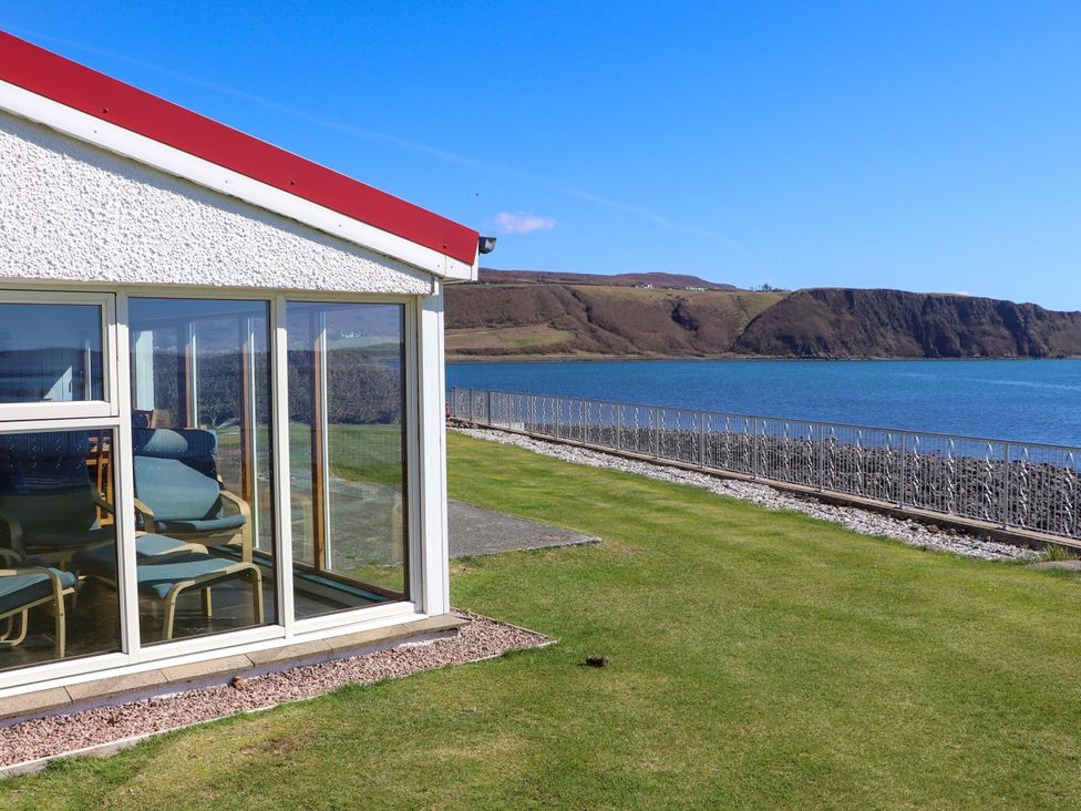 A garden with a glass wall and chairs at Jubilee Cottage Uig