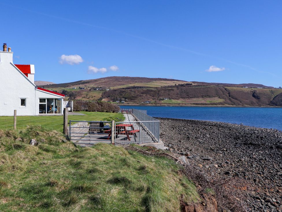 A house by the water with a fence and outdoor furniture at Jubilee Cottage Uig