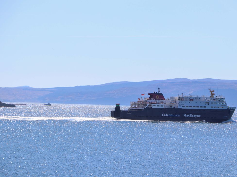 A ferry sailing on the water near hills at Jubilee Cottage Uig
