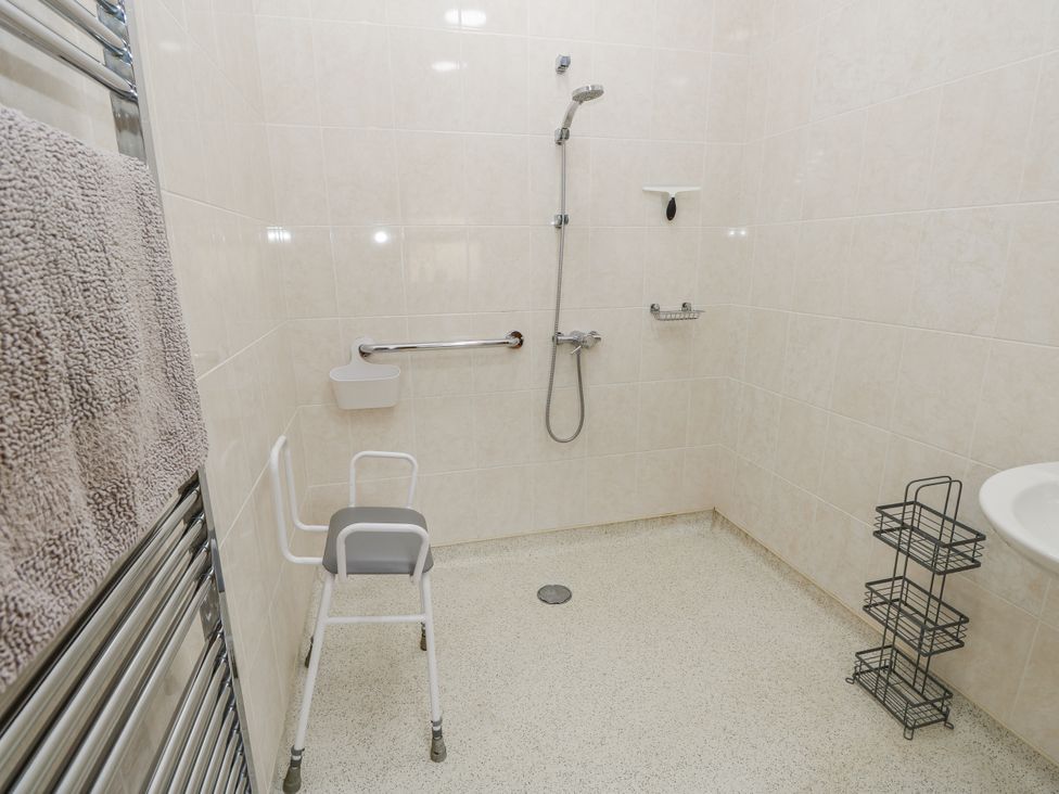 A bathroom with a shower, sink, and grab bars at 2 The Stables, Ryde