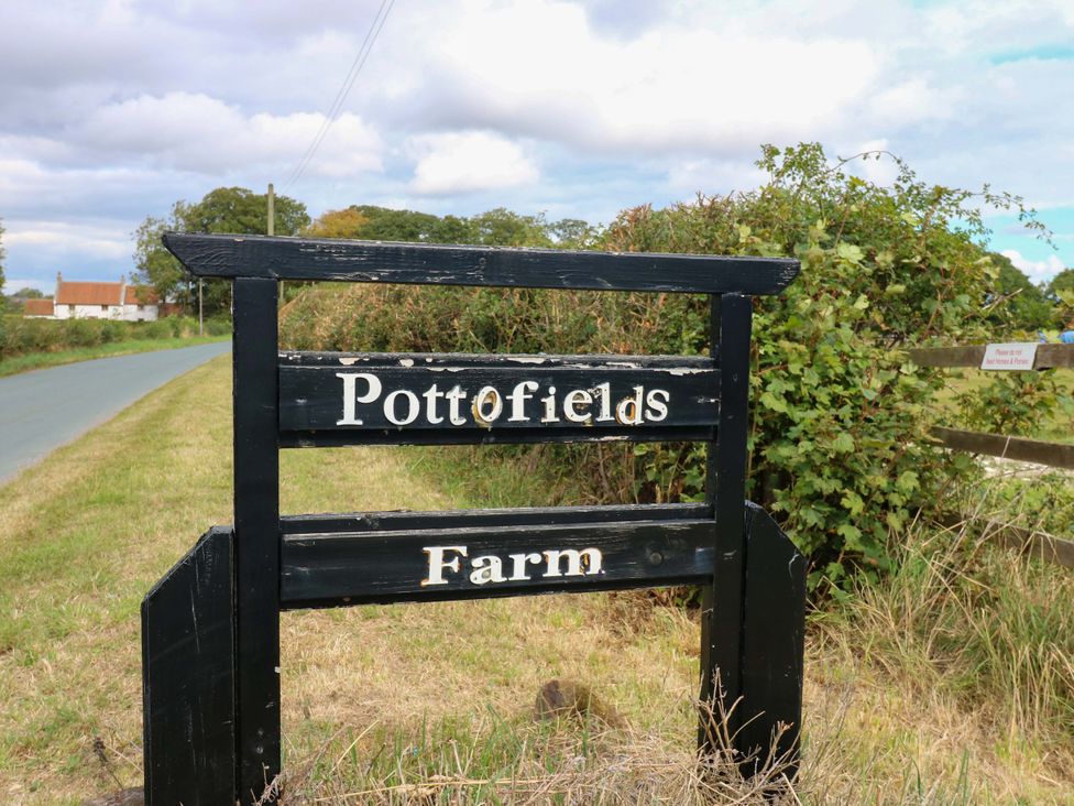 A sign for PottOfields Farm on a road near grass and bushes at Pottowe Cottage in Potto near Stokesley