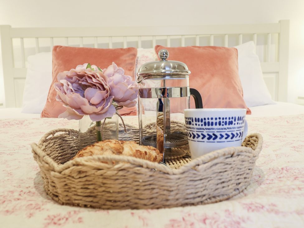 A tray with a coffee maker, cup, flower, and croissant on a bed at Maritime Mews, 6 The Oakleys, Porthmadog