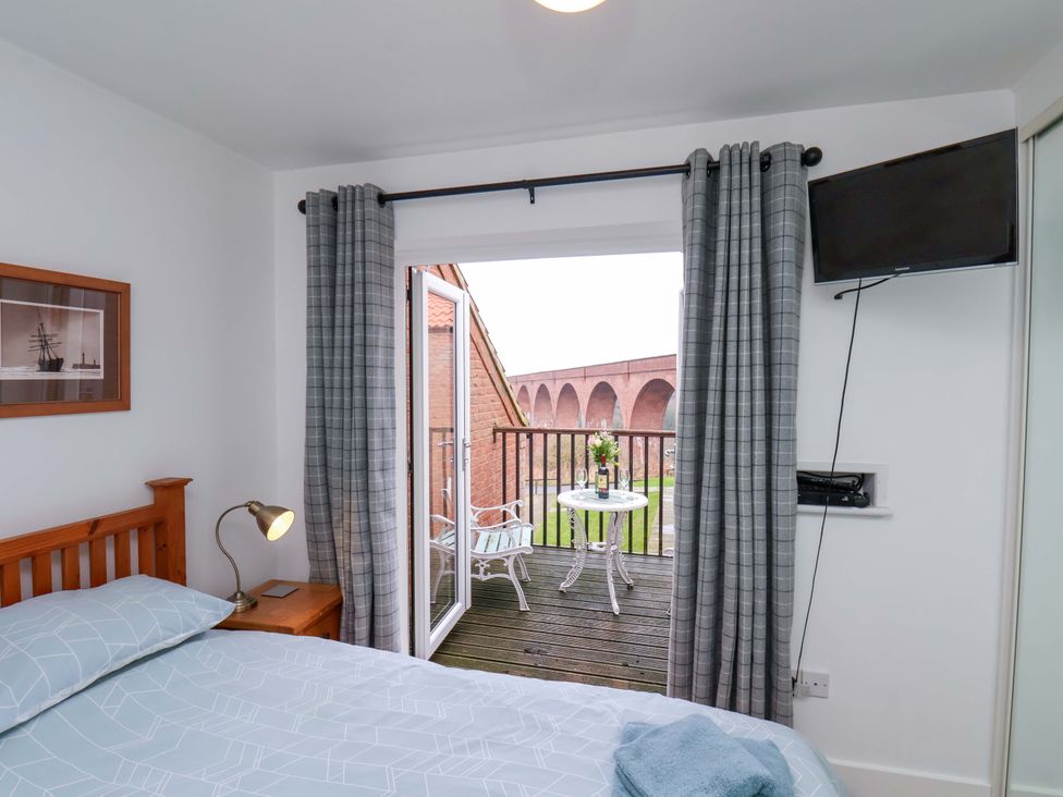 A bedroom with a balcony and television at Berry Banks Cottage in Whitby