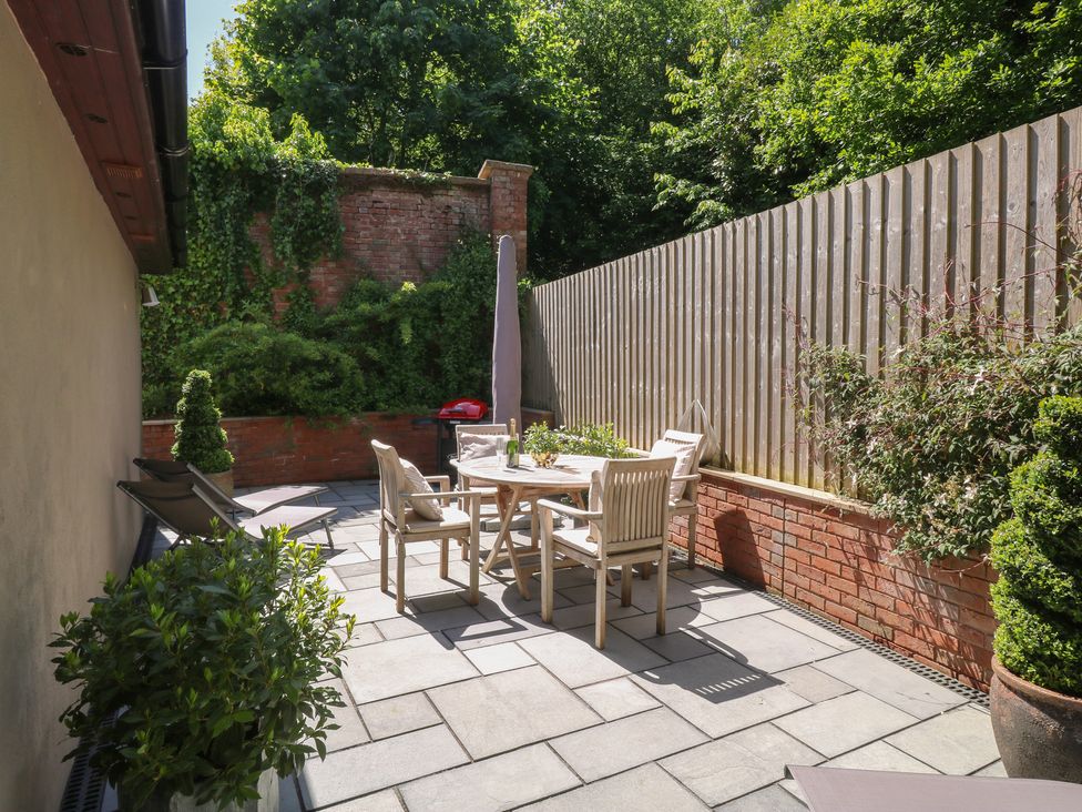 An outdoor patio with a round wooden table and four chairs two lounge chairs plants a brick wall and a wooden fence at Treetops in Southerton