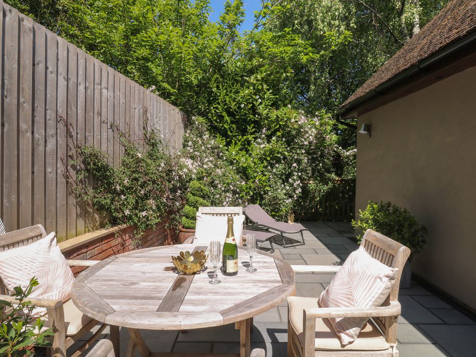 An outdoor patio with a round wooden table and four chairs with cushions a bottle and glasses on the table two sun loungers and plants against a wooden fence at Treetops in Southerton