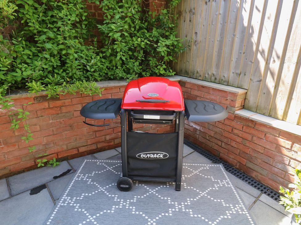 A red barbecue grill on a patterned outdoor rug in a corner with brick walls and green plants at Treetops in Southerton
