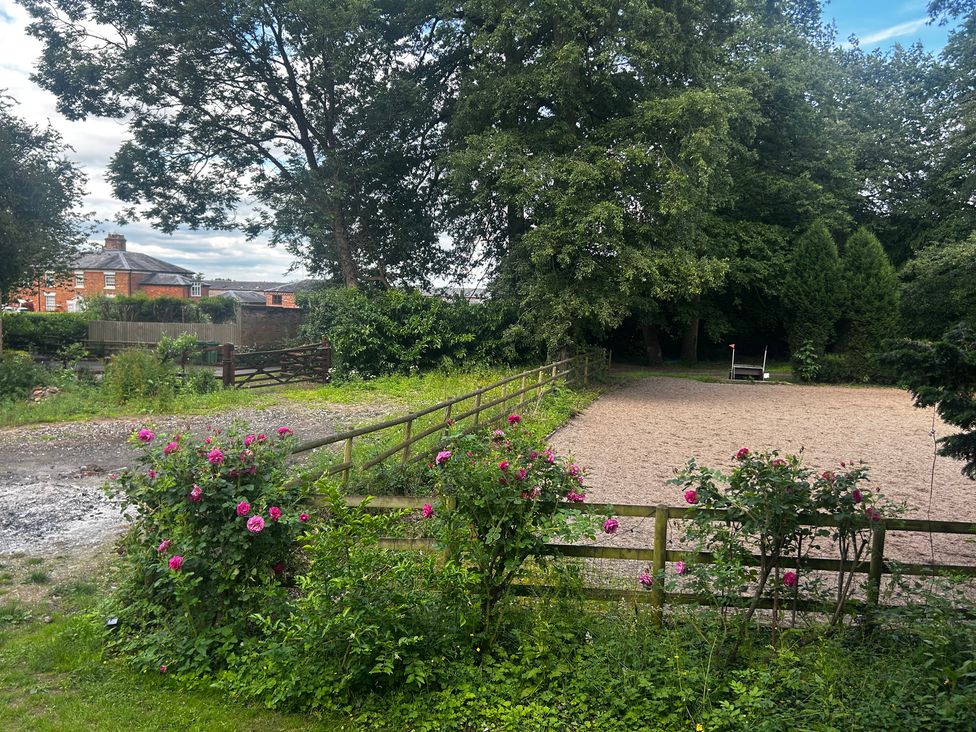 An outdoor area with trees, flowers, and a sand arena at Shrewsbury Lodge Ingestre near Great Haywood