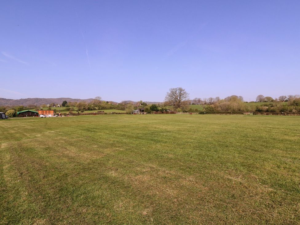 A large grassy field with trees and a building at The Turbles - Swallows Nest Castlemorton near Welland