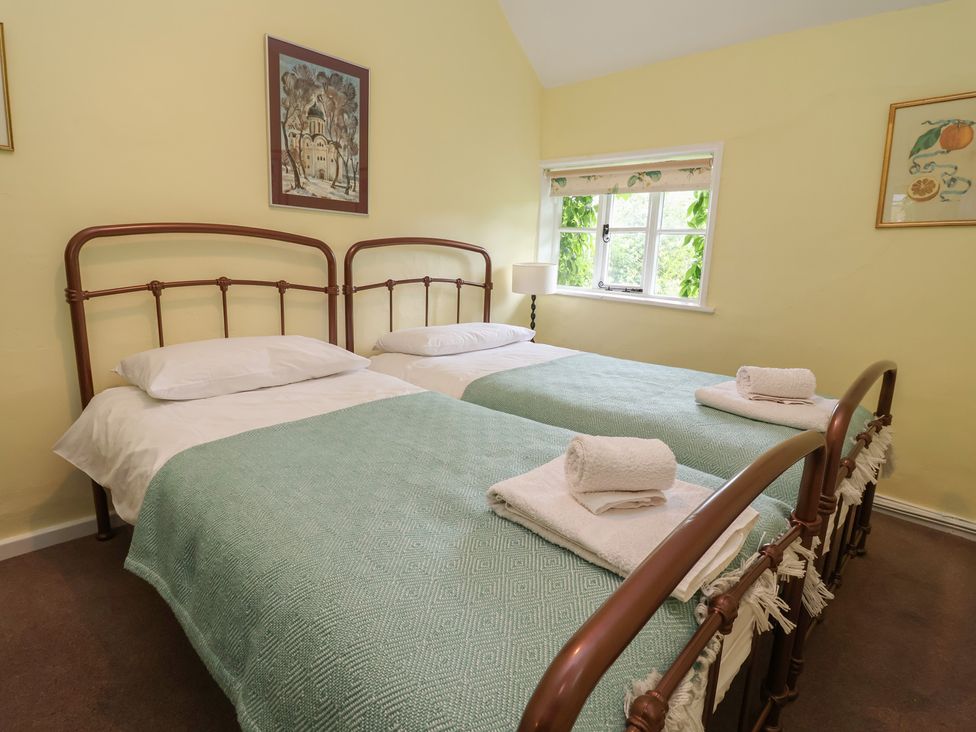 A bedroom with two beds, a lamp and window at Wolvesacre Mill Cottage in Agden near Whitchurch