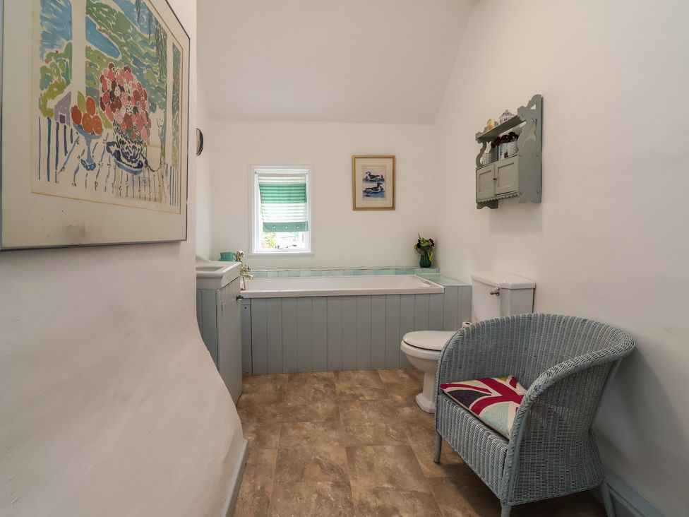 A bathroom with a bathtub, toilet, and chair at Wolvesacre Mill Cottage in Agden near Whitchurch