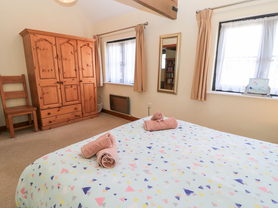 A bedroom with a bed, wardrobe, chair, and mirror at Corner Barn Winterborne Stickland