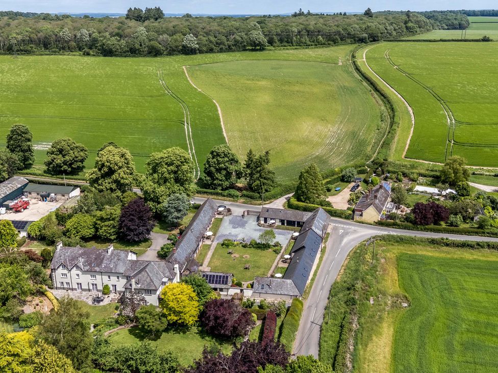 An aerial view of a house and barns surrounded by fields and trees at Corner Barn Winterborne Stickland