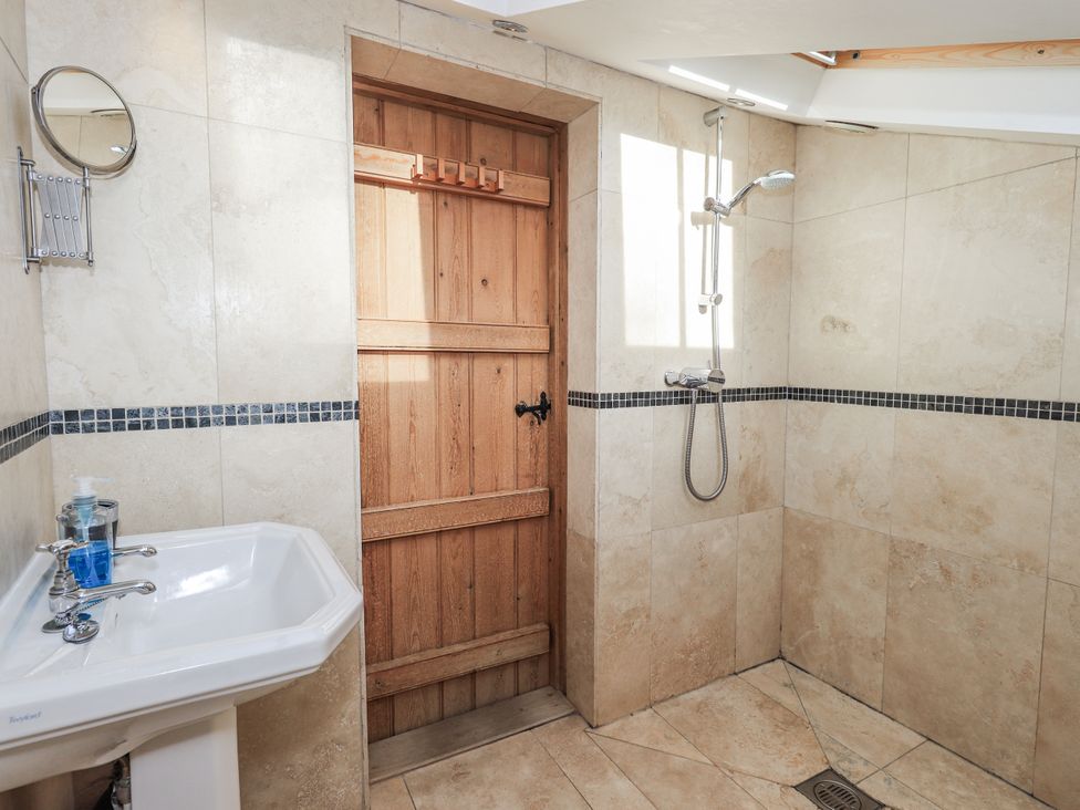 A bathroom with a sink, shower and wooden door at Usherwoods Dairy, Tatham