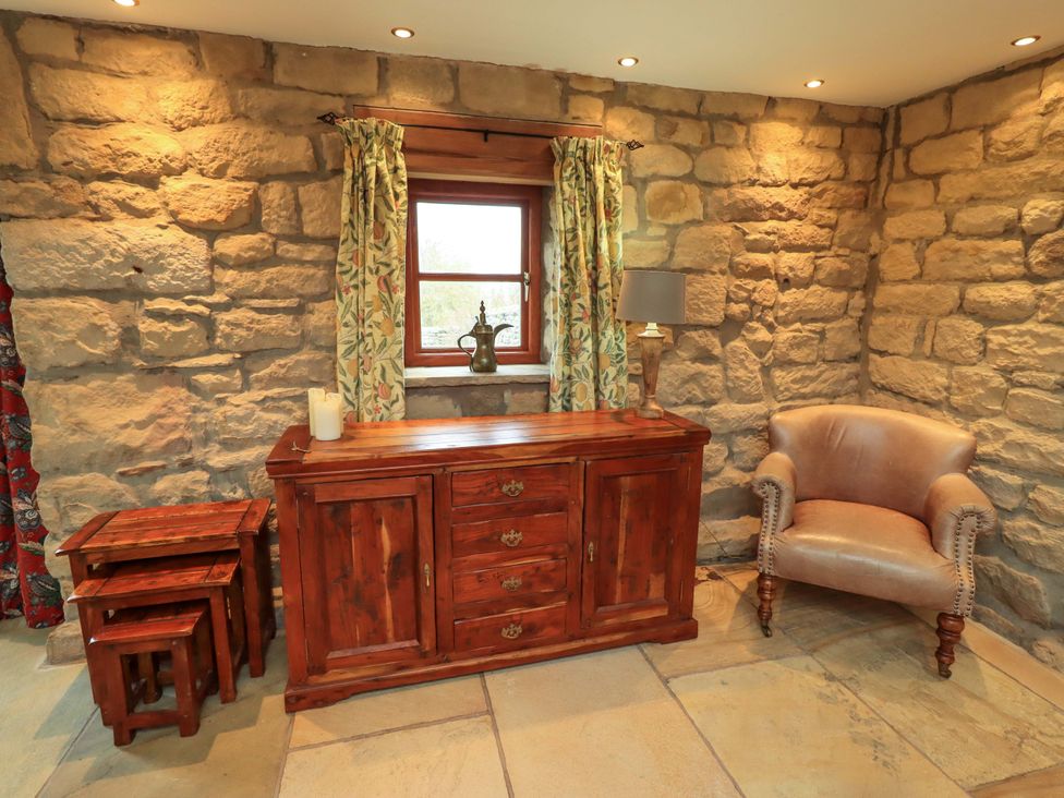 A living room with a stone wall and wooden furniture at Usherwoods Barn in Tatham