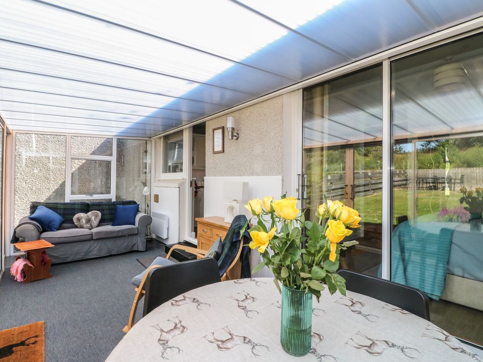 A conservatory with a sofa and flowers on a table at Steam Cottage in Aviemore