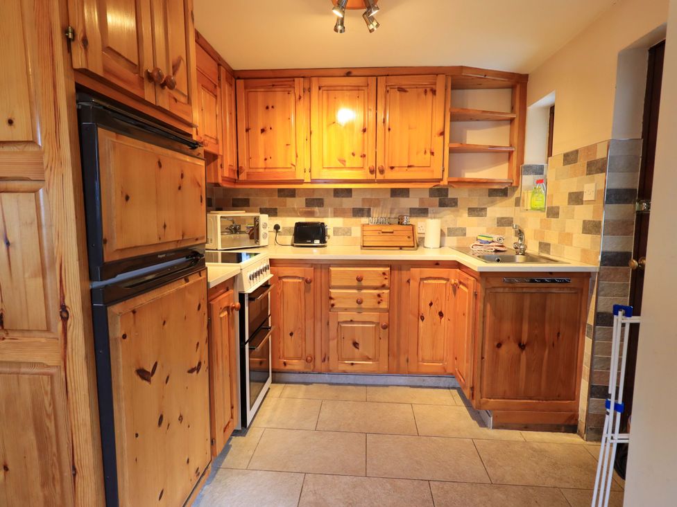 A kitchen with wooden cabinets and appliances including a refrigerator and microwave at Ghyll Bank Bungalow Staveley near Windermere