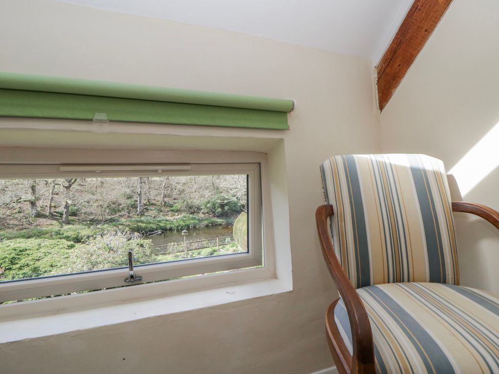 A chair next to a window overlooking a natural view at Gardener's Cottage Llanwrthwl near Rhayader