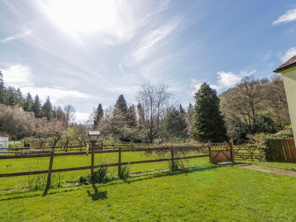A garden with grass, trees, and a fence at Gardener's Cottage Llanwrthwl near Rhayader