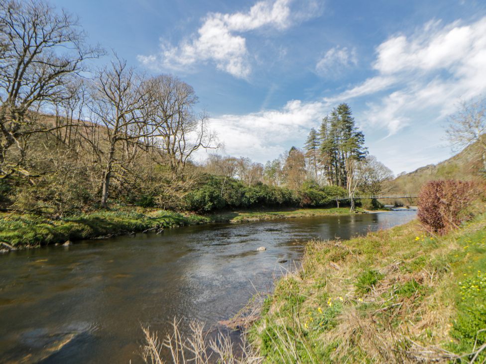 A river bordered by trees and grass at Gardener's Cottage in Llanwrthwl near Rhayader