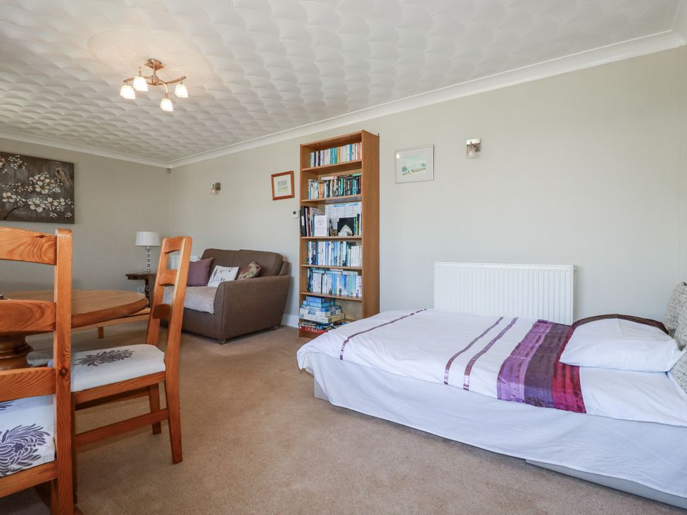 A living room with a table and chairs next to a sofa and bookshelf at Jenny Wren in Tywardreath near Fowey