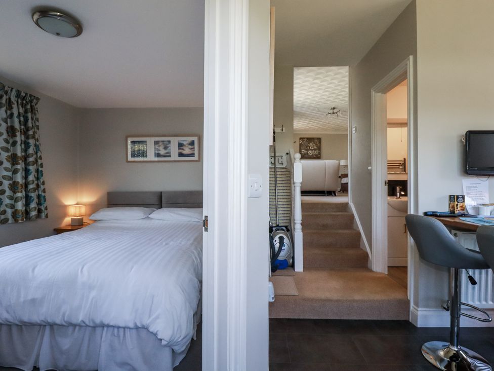 A bedroom with a bed and lamp leading to stairs at Jenny Wren in Tywardreath near Fowey