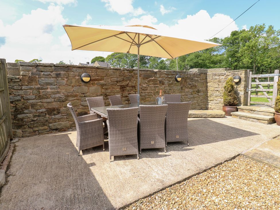 An outdoor patio with a table and chairs under an umbrella at Bullace Barn Millhouse Green