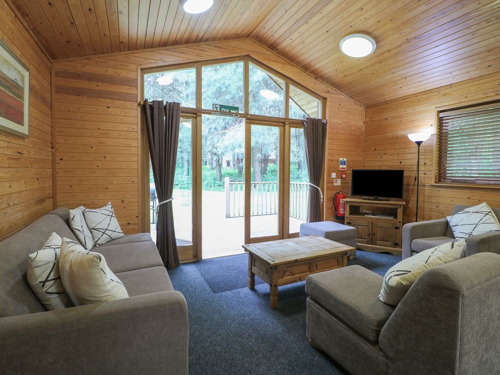 A living room with a sofa set, wooden coffee table, television on a cabinet, and large glass doors at Birch Lodge in Rosliston