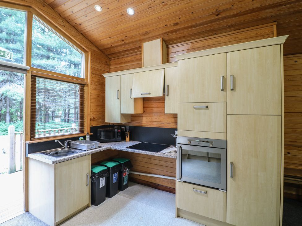 A kitchen with wooden cabinets a sink a microwave an oven and three trash bins at Birch Lodge in Rosliston