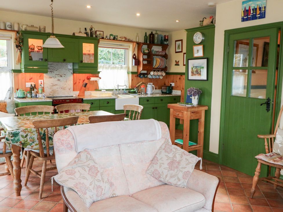 A kitchen with cabinets and a dining table at Herons Cove Cottage in Ballydehop