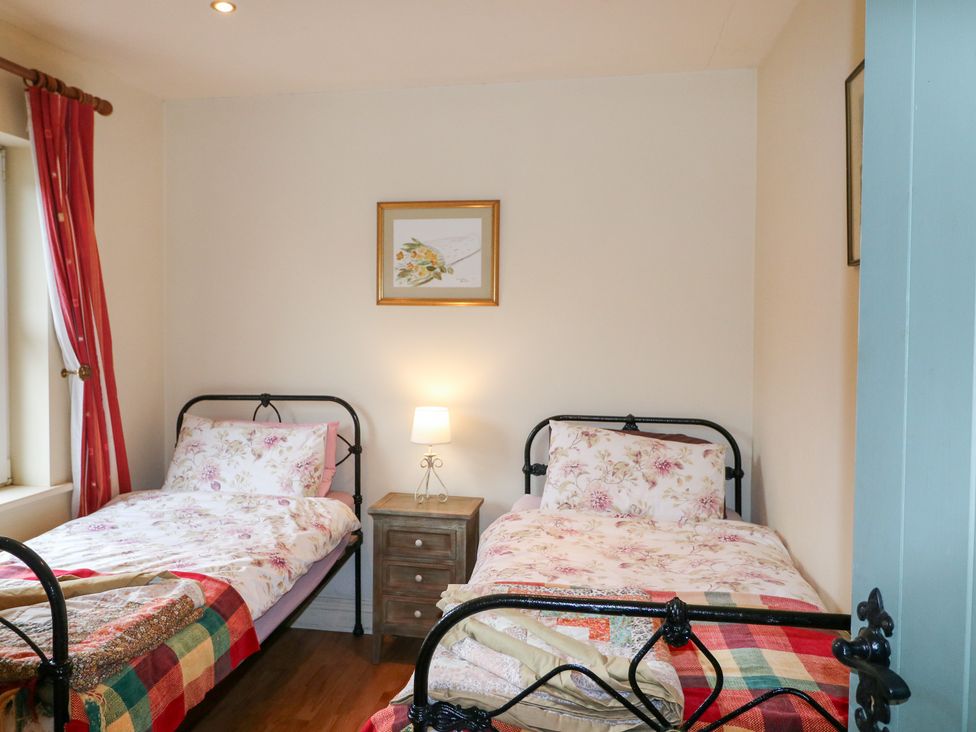 A bedroom with two beds and a bedside table at Herons Cove Cottage in Ballydehop