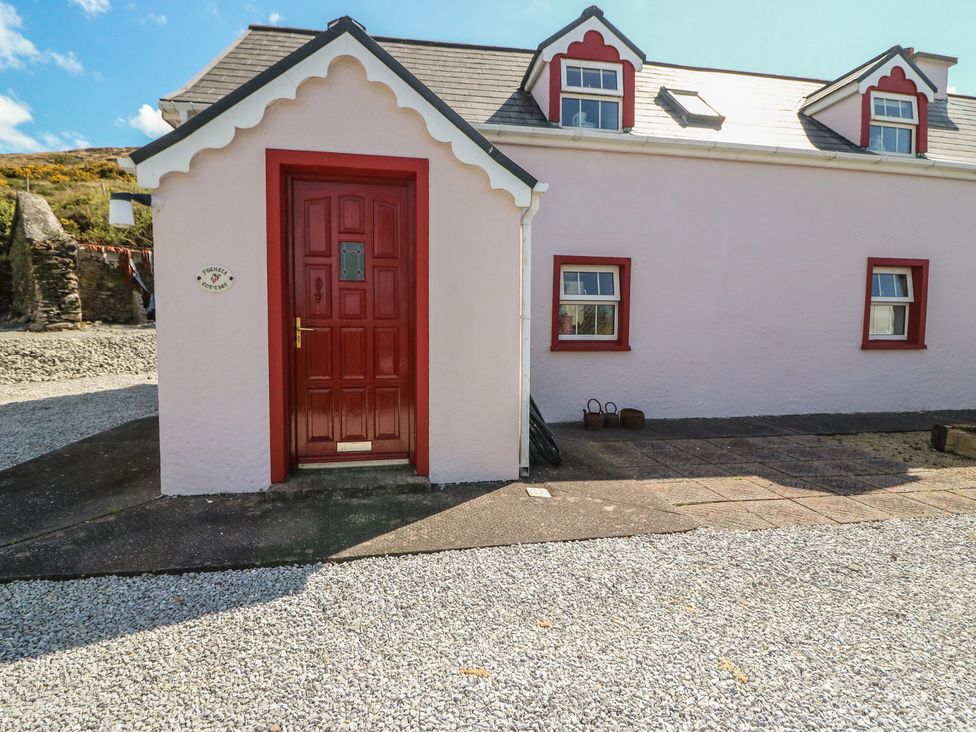 A pink exterior of a cottage with a red door at Fuschia Cottage, Waterville, County Kerry