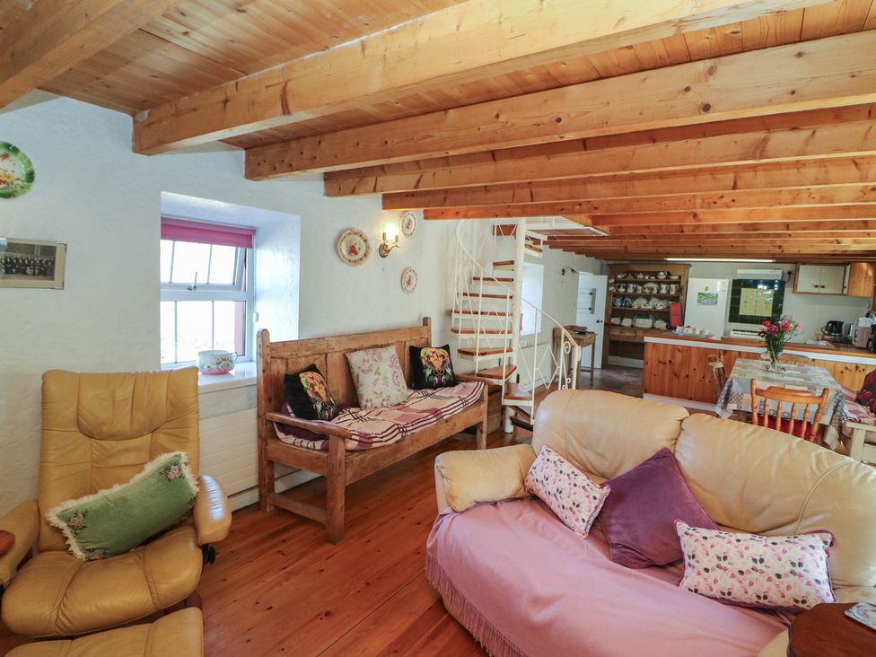 A living room featuring a sofa, chairs, wooden bench, and a staircase at Fuschia Cottage in Waterville, County Kerry