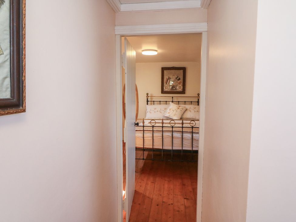 A corridor leading to a bedroom with a bed and paintings at Fuschia Cottage, Waterville, County Kerry