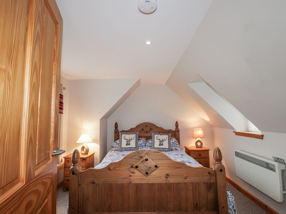 A bedroom with a wooden bed, nightstands and lamps at The Croft House in Muir of Ord near Beauly