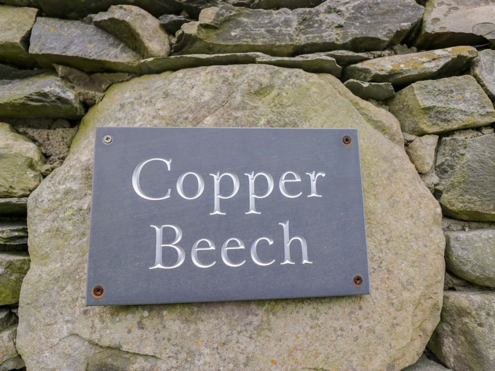 A sign reading Copper Beech mounted on a stone wall at Copper Beech Cottage in Torver