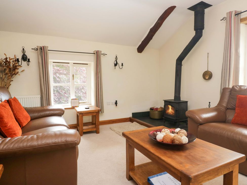 A living room with a wood burning stove and seating at Copper Beech Cottage in Torver