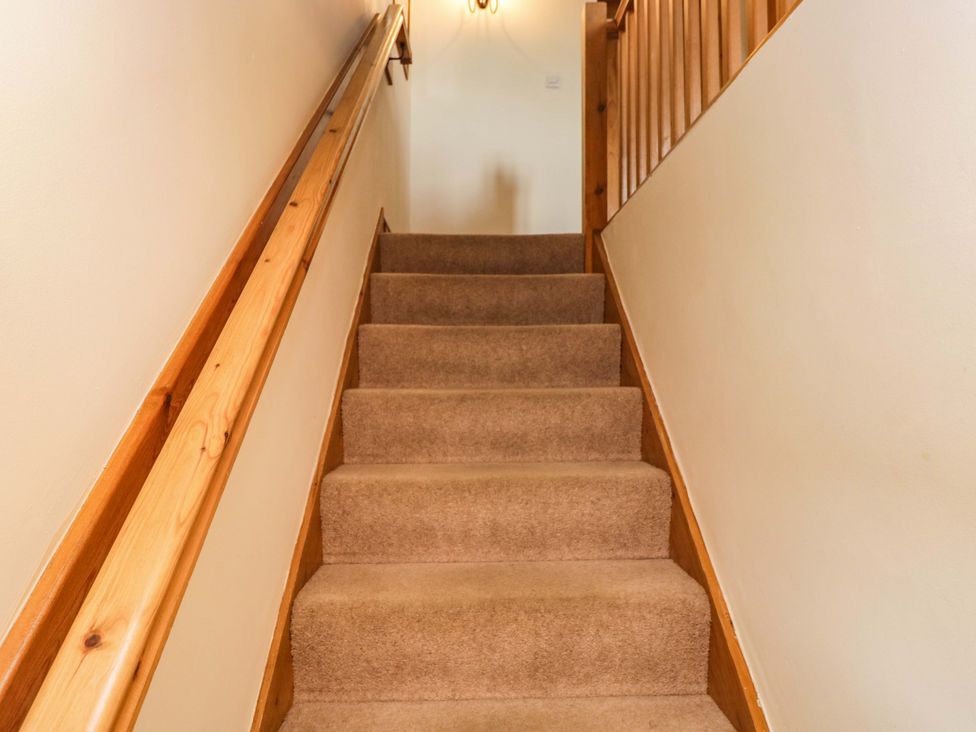 A staircase with carpet and wooden handrail at Copper Beech Cottage Torver