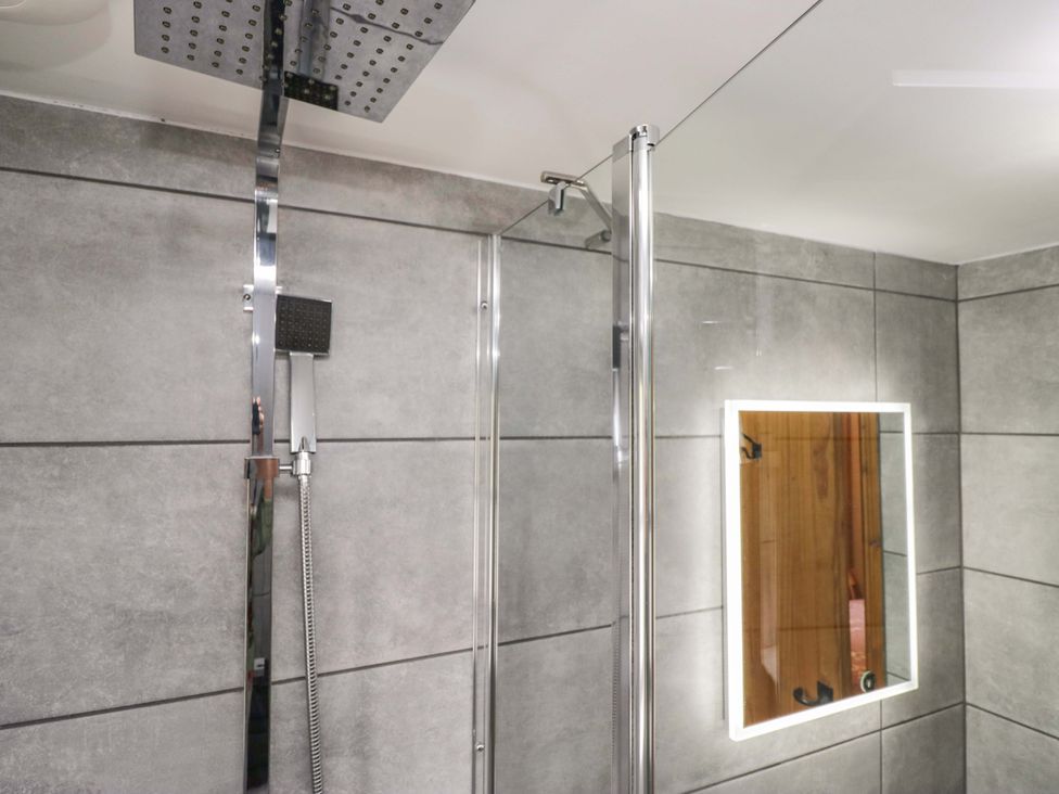 A bathroom with a shower and mirror at Copper Beech Cottage in Torver