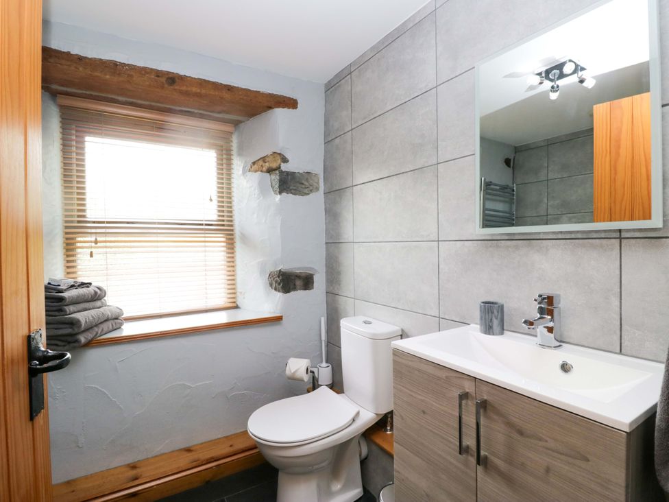 A bathroom with a toilet, sink, and window at Copper Beech Cottage in Torver