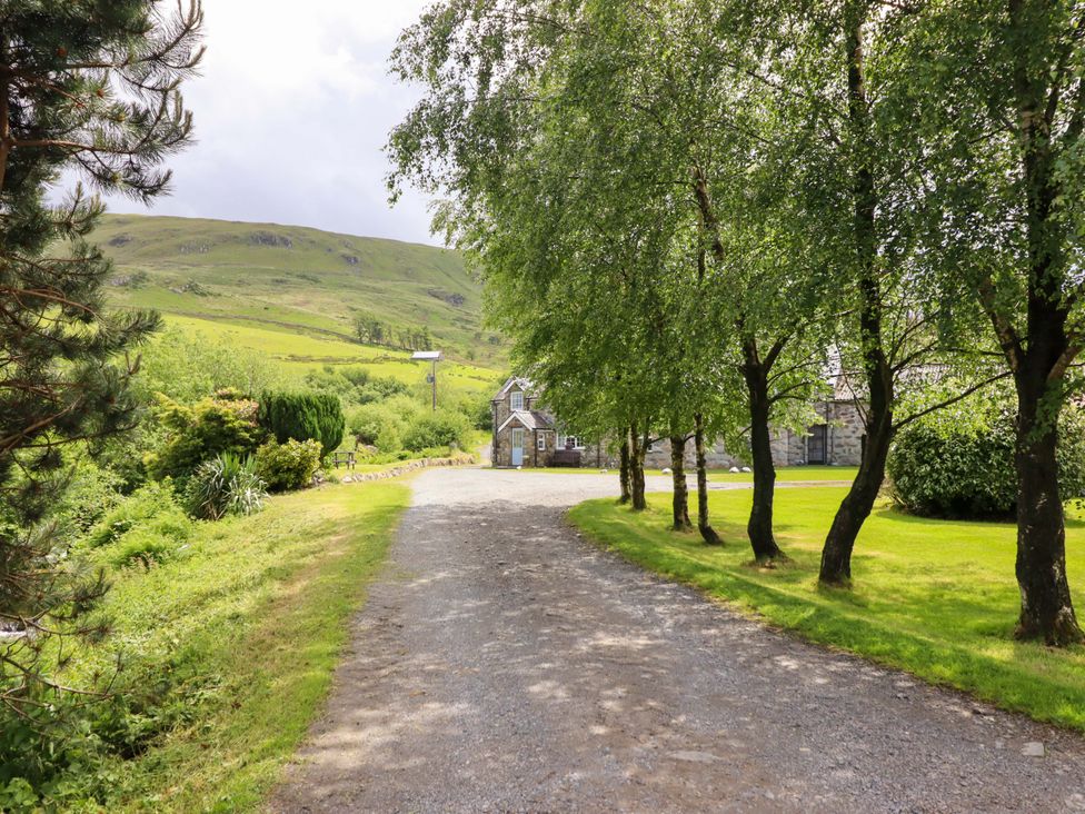 A gravel path lined with trees leading to a building at Stabal Cottage in Dolgellau