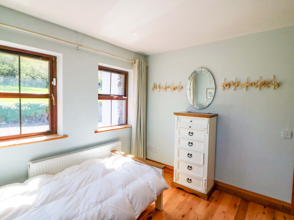 A bedroom with windows, a bed, and a chest of drawers at Stone Cottage in Waterville, County Kerry