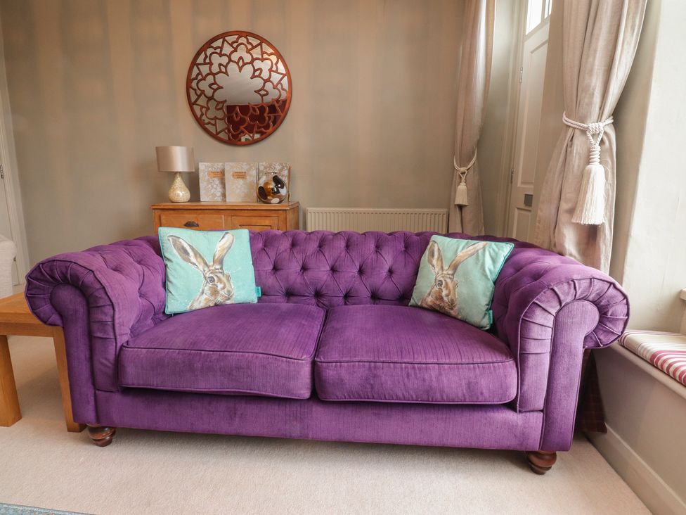 A living room with a purple sofa and cushions at Canalside Cottage in Farnhill near Skipton