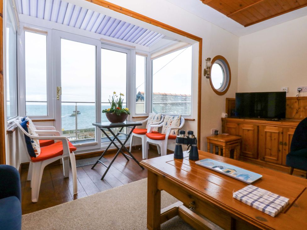 A sunroom with a table and chairs overlooking the sea at Min Y Traeth in Bull Bay