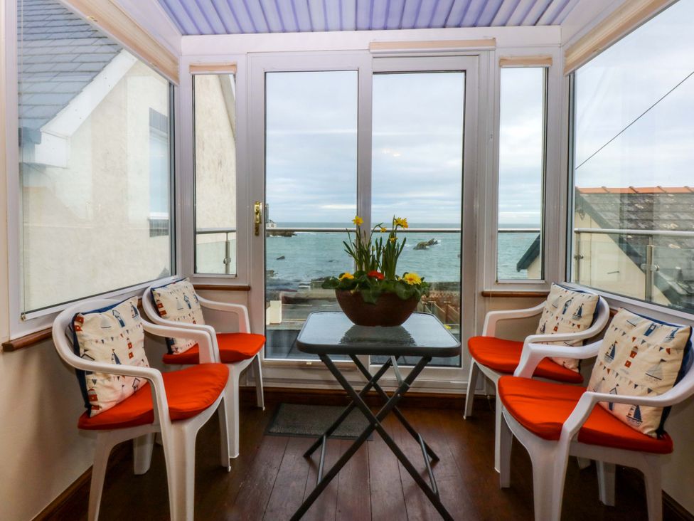 A conservatory with chairs and a table overlooking the sea at Min Y Traeth in Bull Bay