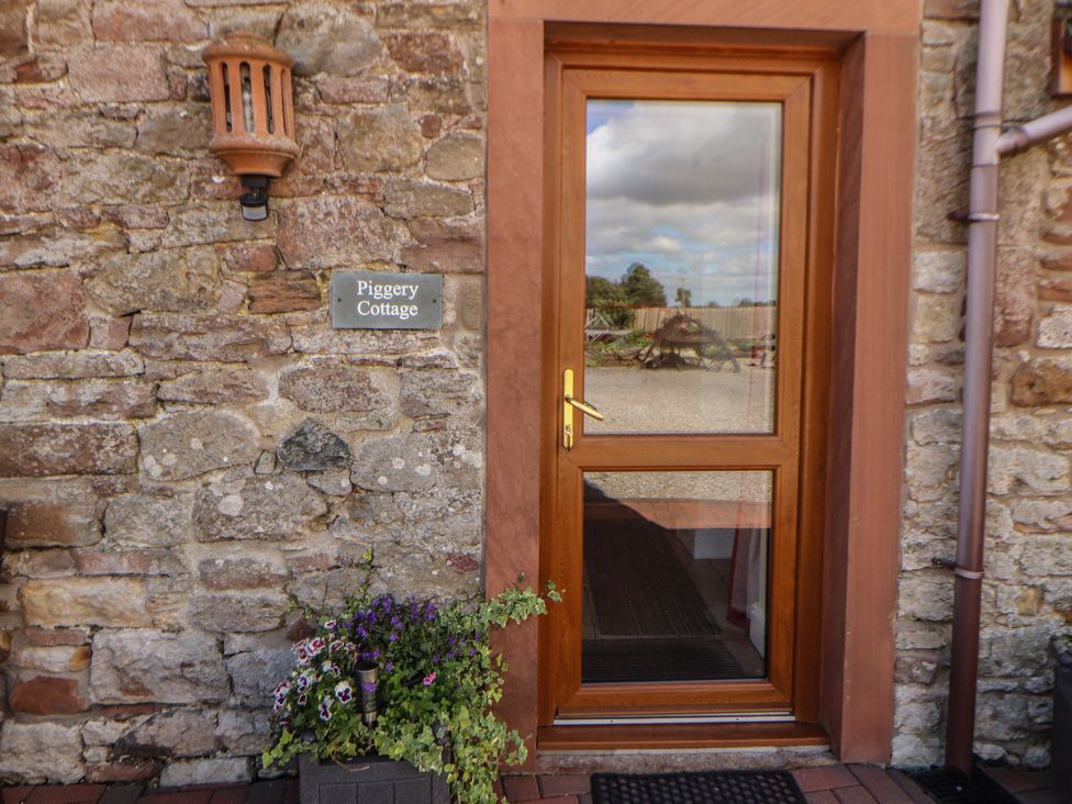 An entryway with a wooden door and flower pot at Piggery Cottage Wigton